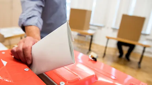 Ein Wahlhelfer steckt in einem Wahllokal einen Stimmzettel in eine Wahlurne.