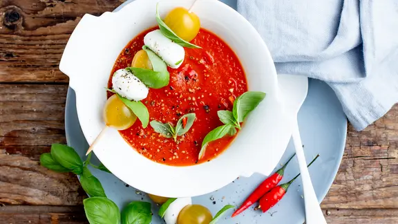 Ein tiefer Teller mit Tomatenkaltschale, darauf Mozzarella-Spieße und Basilikumblätter.