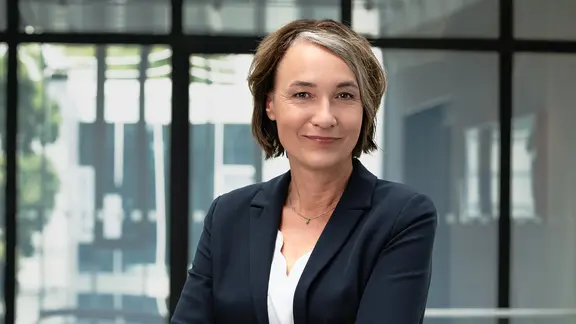 Eine Frau mit kurzen braunen Haaren blickt mit leichtem Lächeln in die Kamera.
