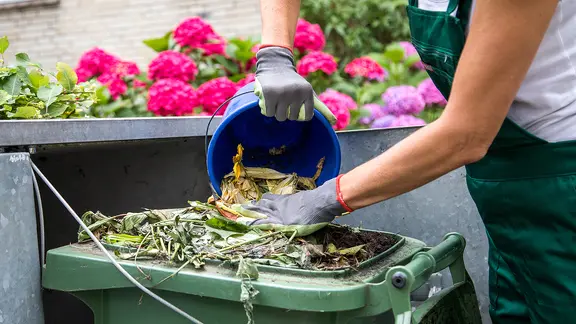 Eine Person entsorgt am Biomüll in der grünen Tonne.