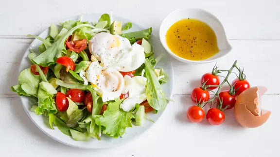Ein Teller mit Salat und porchierten Eiern steht auf einem Tisch.