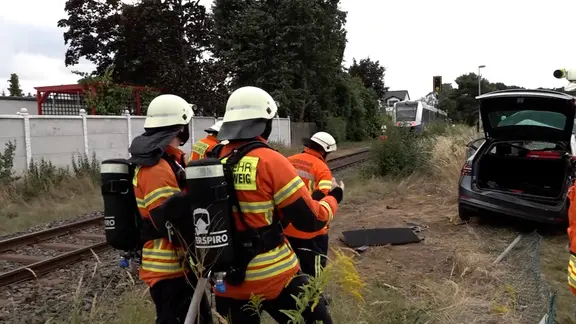 Einsatzkräfte der Feuerwehr stehen vor einer Unfallstelle an einem Bahnübergang.