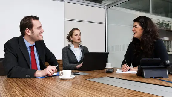 Besprechung im Büro: Drei Personen sitzen an einem Tisch.