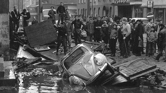 Menschen schauen bei der Bergung eines VW Käfer zu nach der Sturmflut 1962 in Hamburg-Wilhelmsburg.