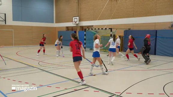 Zwei Mannschaften spielen in einer Halle Hockey