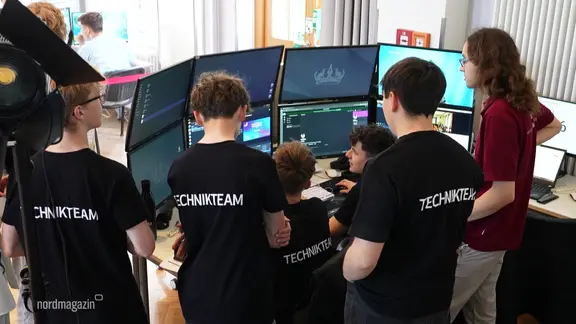 Eine Gruppe junger Menschen schart sich um Computerbildschirme. Auf ihren T-Shirts steht "Technikteam".