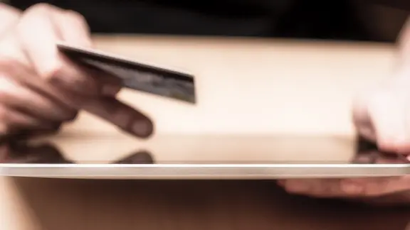 Eine Hand hält eine Bankkarte, die andere tippt auf einem Tablet.