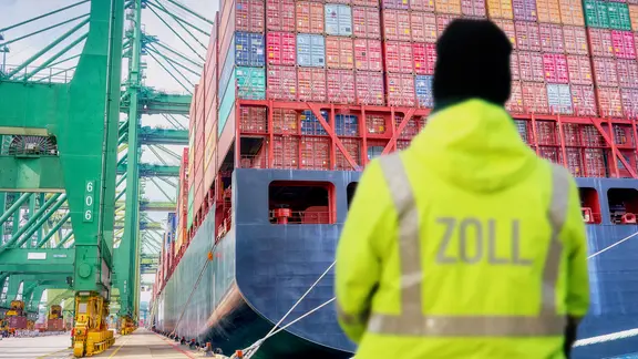 Person von hinten in gelber Leuchtjacke mit der Aufschrift Zoll - unscharf.