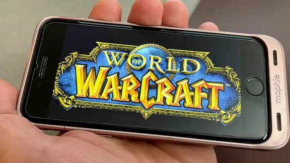 Eine Hand hält ein Smartphone, auf der das Logo vom Computerspiel "World of Warcraft" zu sehen ist.