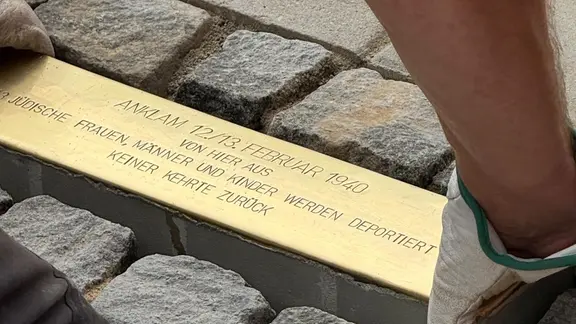 Eine messingfarbene Platte wird in einen Gehweg gelegt