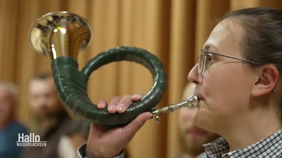 Eine Person mit Brille spielt ein grünes Jagdhorn.