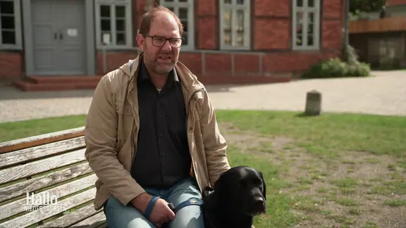 Ein Mann sitzt auf einer Bank und hält einen Hund fest.
