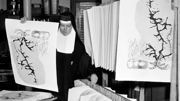 Sister Mary Corita, alias Corita Kent, trägt Drucke im Atelier
