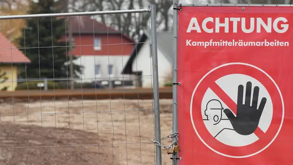 Ein Schild mit der Aufschrift "Achtung Kampfmittelräumarbeiten" an einer Baustelle.