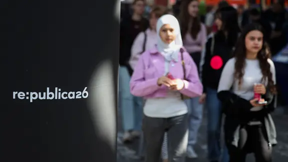 Zwei junge Frauen gehen an einem Schild vorbei, auf dem "re:publica26" steht. 