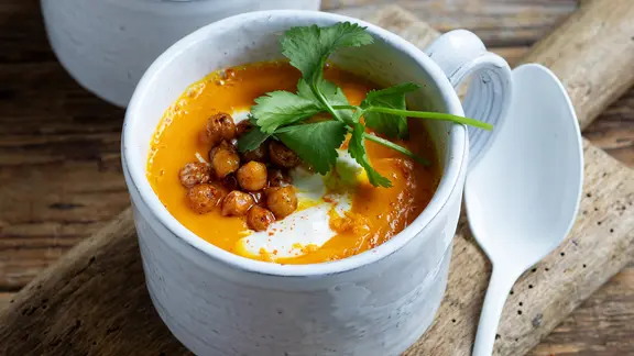 Eine Suppenschale mit einer Kürbsissuppe, garniert mit gebackenen Kichererbsen.