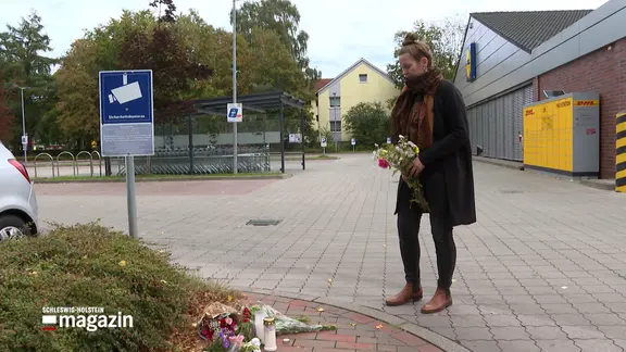Eine Frau legt vor einem Supermarkt Blumen nieder