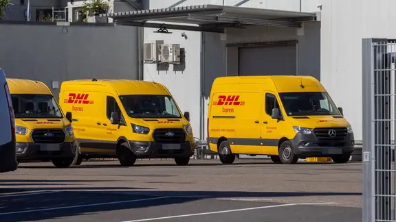 Fahrzeuge von DHL stehen auf einem Firmengelände.