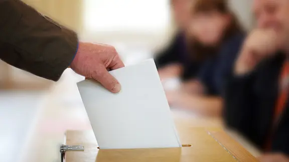 Hand wirft Umschlag in Wahlurne