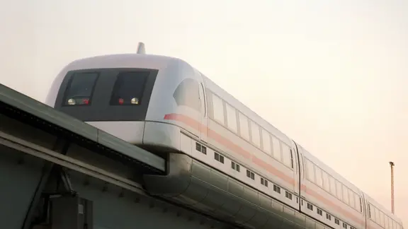 Eine weiße Hochbahn fährt auf einer erhöhten Schiene unter hellem Himmel.