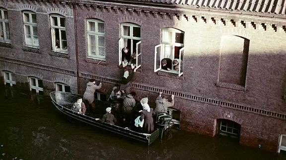 Helfer retten ein Kind per Boot aus einem eingeschlossenen Wohnhaus im überschwemmten Hamburg-Wilhelmsburg 1962