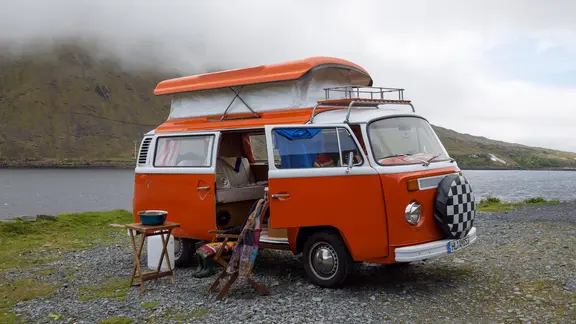 Ein alter VW-Bulli mit Campingausstattung steht an einem See.