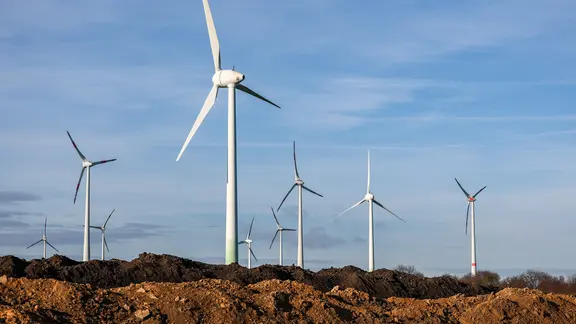 Windräder stehen hinter Erdhaufen am Rande eines Baufelds.