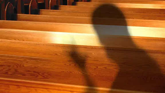 Montage: Bedrohlicher Schatten vor Kirchenbänken.