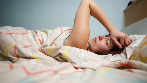 Eine Frau liegt im Bett und greift sich an den Kopf.