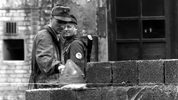 Ein Bauarbeiter errichtet am 18. August 1961 unter der Aufsicht eines Volkspolizisten an der Sektorengrenze am Potsdamer Platz eine mannshohe Mauer.