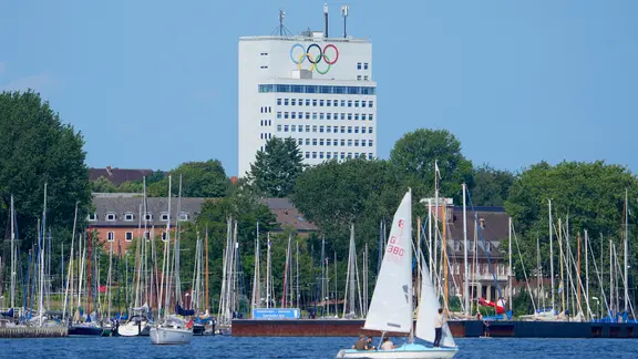 Blick auf Segelboote in der Kieler Förde. Im Hintergrund ein Haus mit den Olympischen Ringen.