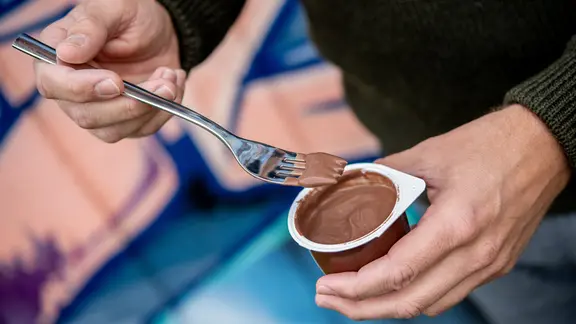  Ein junger Mann isst einen Schokoladenpudding mit einer Gabel.