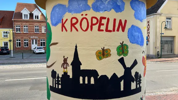 Auf einer Säule am Marktplatz in Kröpelin ist eine gemalte Silhouette der Stadt zu sehen. (ndrde)