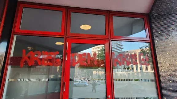 Der mit roter Farbe gemalte Schriftzug "Krieg dem Krieg" steht auf einer Fensterscheibe.