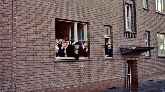 Menschen schauen aus einer Wohnung im überschwemmten Hamburg-Wilhelmsburg 1962.