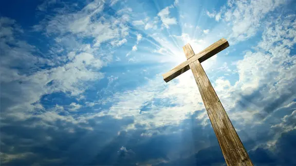 Ein Holzkreuz vor einem wolkigem Himmel.
