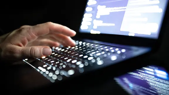 Eine Person tippt mit den Fingern auf einer beleuchteten Laptop-Tastatur.