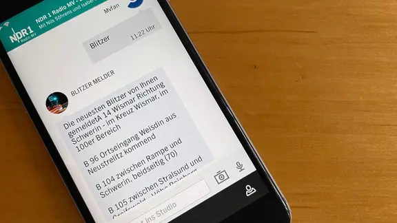 Ein Smartphone zeigt einen Chat in der NDR MV App, in dem die App eine Liste mit Blitzern und Lasern in Mecklenburg-Vorpommern anzeigt.