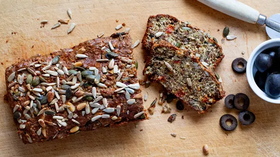 Eiweißbrot und schwarze Oliven auf einem Holzbrett.