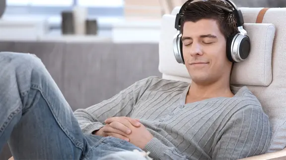 Mann liegt mit geschlossenen Augen und Kopfhörern auf dem Sofa.