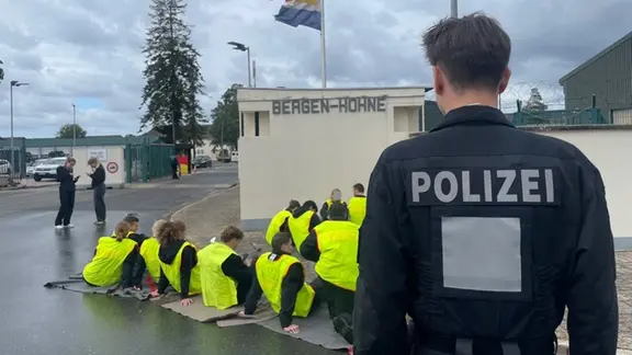 Ein Polizist steht vor Schauspielern, die Demonstranten im Sitzstreik simulieren. 