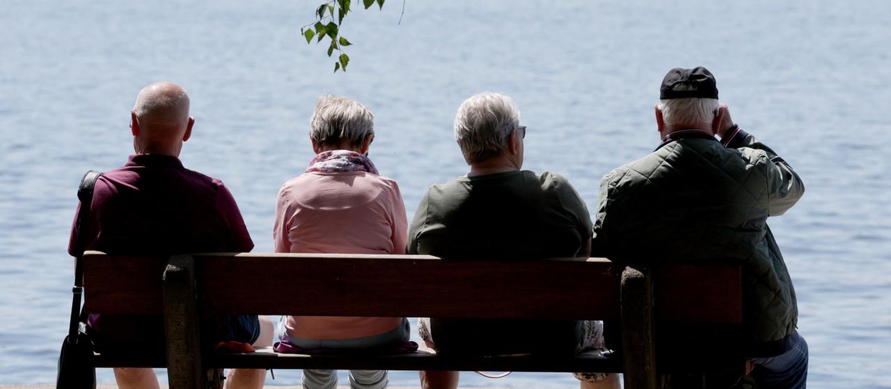 Urlauber und Touristen sitzen bei sommerlichem Wetter auf Bänken am Ufer der Müritz.