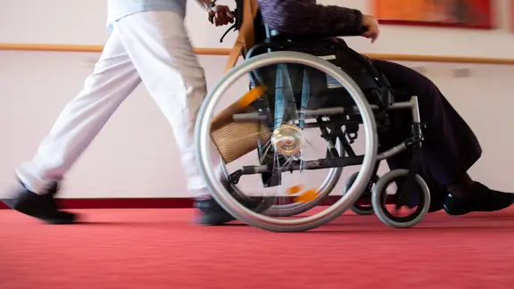 Eine Pflegekraft schiebt einen Pflegebedürftigen in einem Rollstuhl.