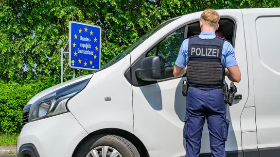 Polizist steht vor einem weißen Lieferwagen an der deutschen Grenze