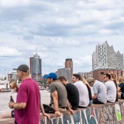 Menschen sitzen in Hamburg auf einer Mauer mit Blick auf die Elbphilharmonie.