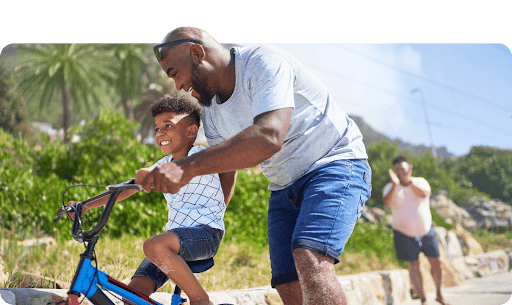 father helping his son ride a bike in the summer time