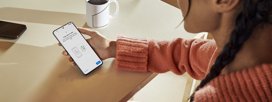 A person sitting at a table with a coffee mug is looking at their phone.