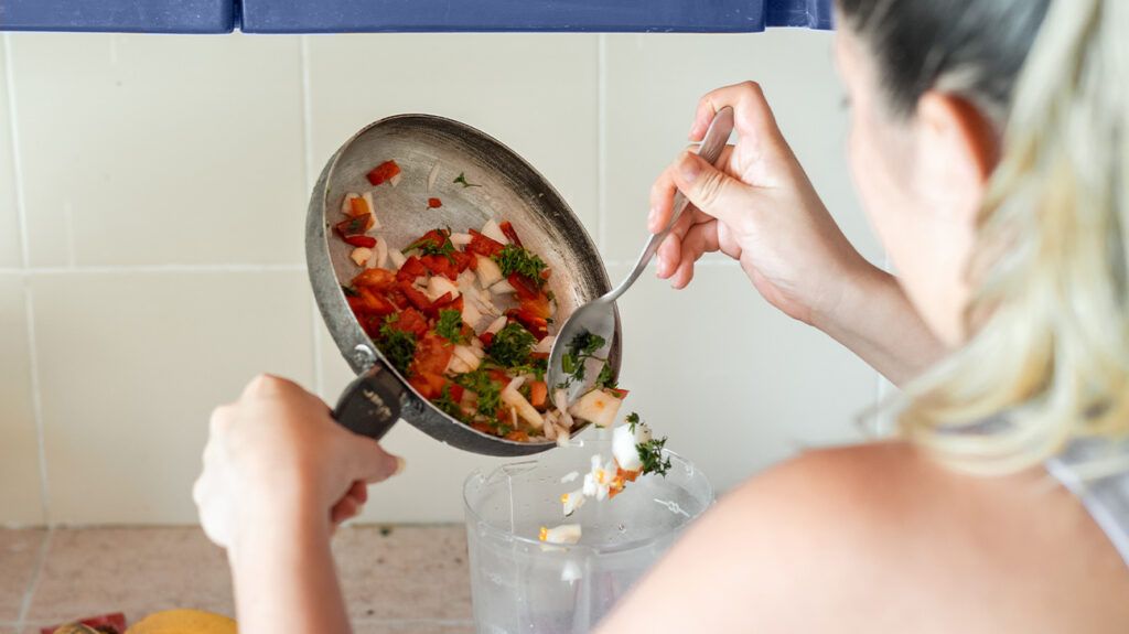 woman adding cooked veggies to a blender
