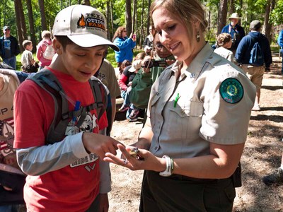 Ranger at park showing boy something in her hand.