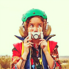 kidjoy: Live version of the girl holding an old camera in front of her face and wearing her full costume ([The Girl])
